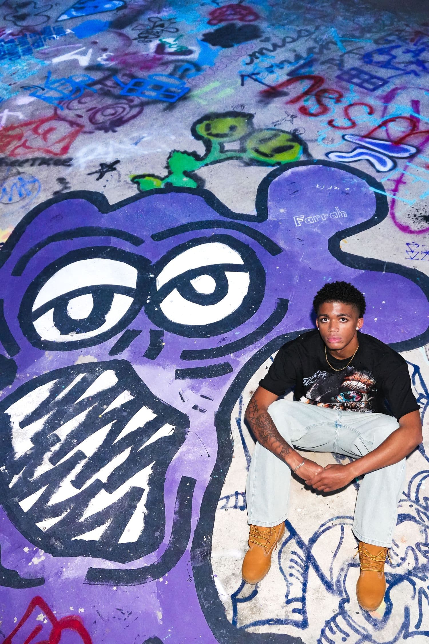 Street portrait on a graffiti-covered floor, the subject seated cross-legged inside a painted cartoon face