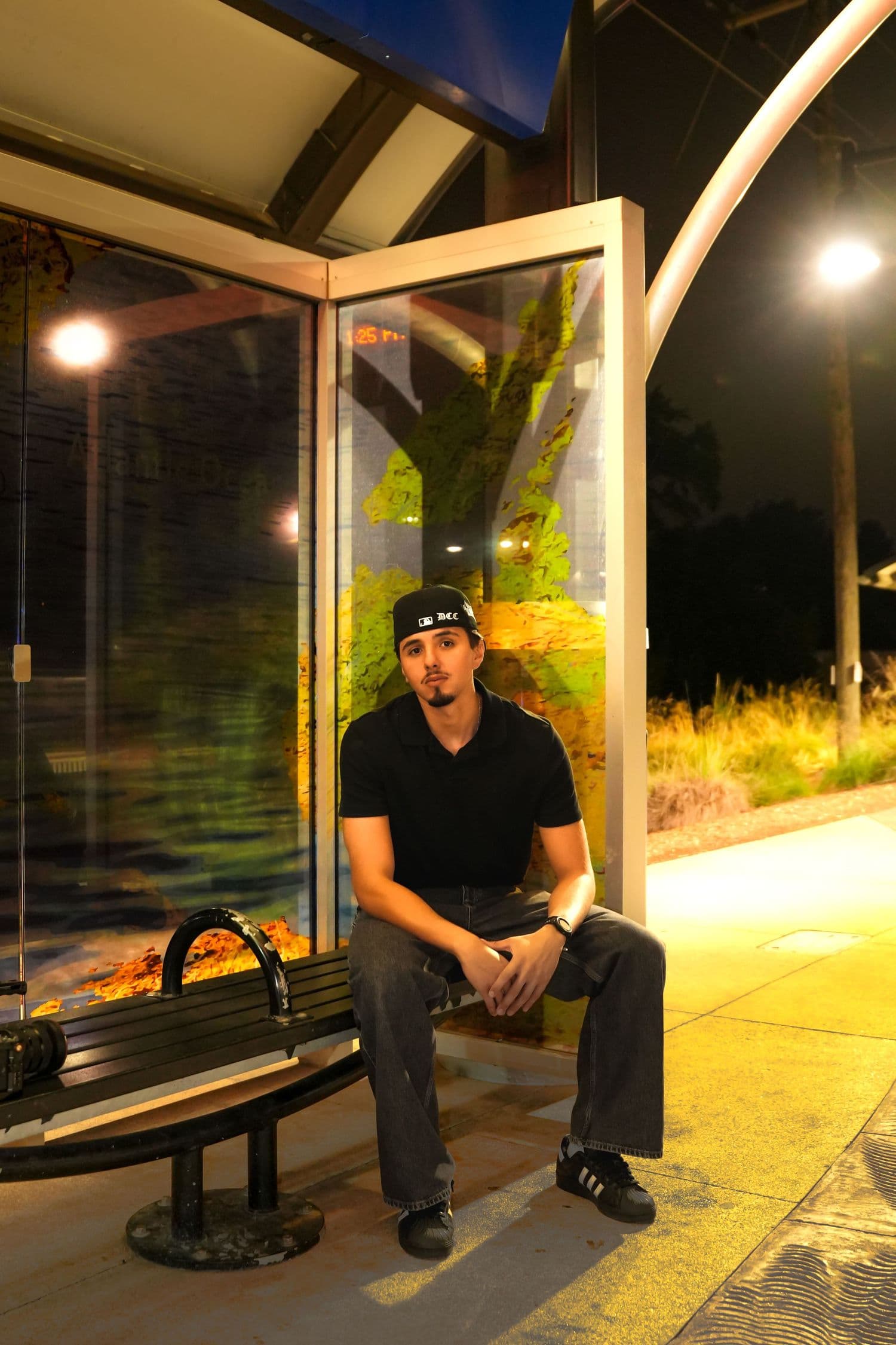 Seated at a bus stop at night, glowing under the shelter lights