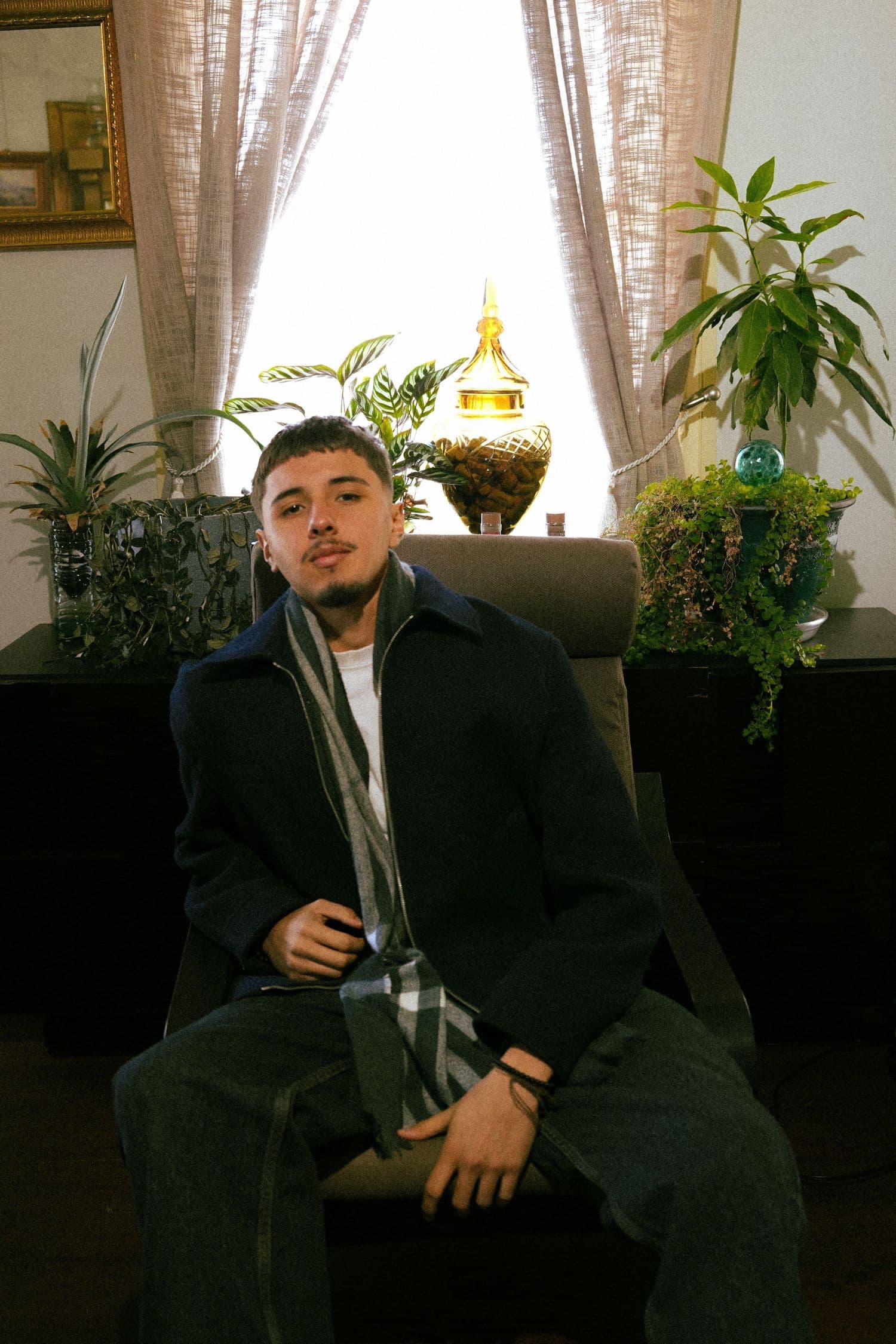 Dark coat and scarf in a living room framed by plants and window light