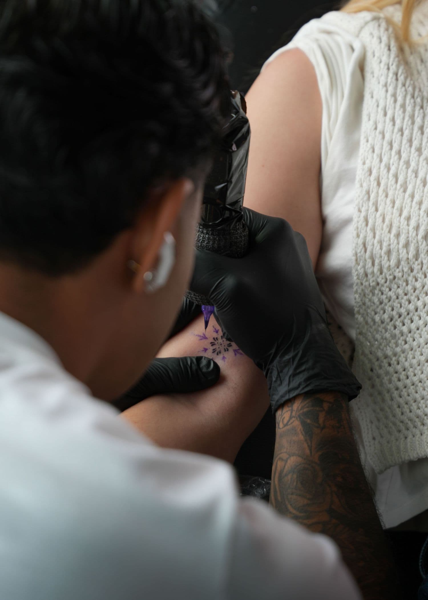 Tattoo artist in black gloves working on a client’s arm